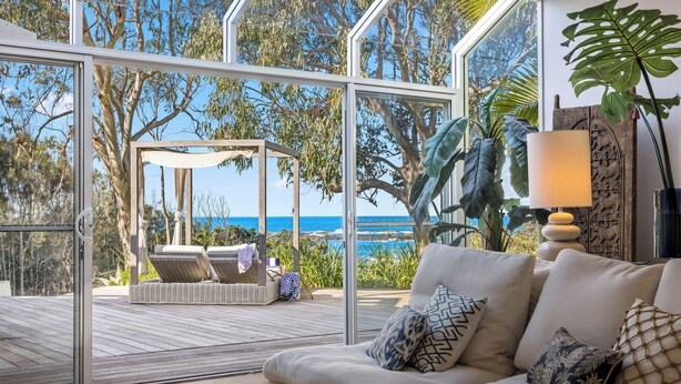 A modern living room with a large glass door leading to a deck overlooking the ocean.