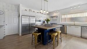 A modern kitchen with stainless steel appliances, a central island with stools, and pendant lighting.