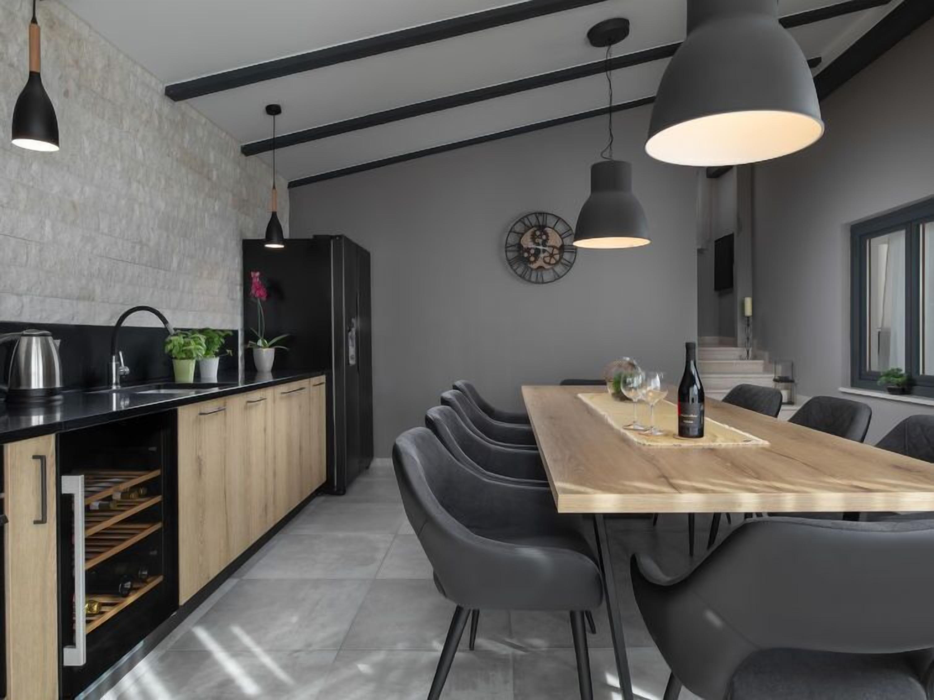 A modern kitchen with a wooden dining table, black chairs, and pendant lights.