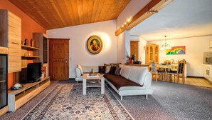 Un salon chaleureux avec un canapé, un téléviseur, des étagères en bois et un coin repas comprenant des chaises et une table.