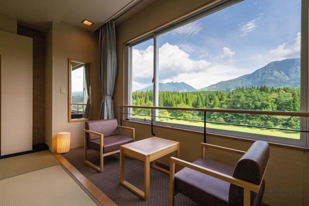 A hotel room with a large window, a sofa, a table, and a mirror.