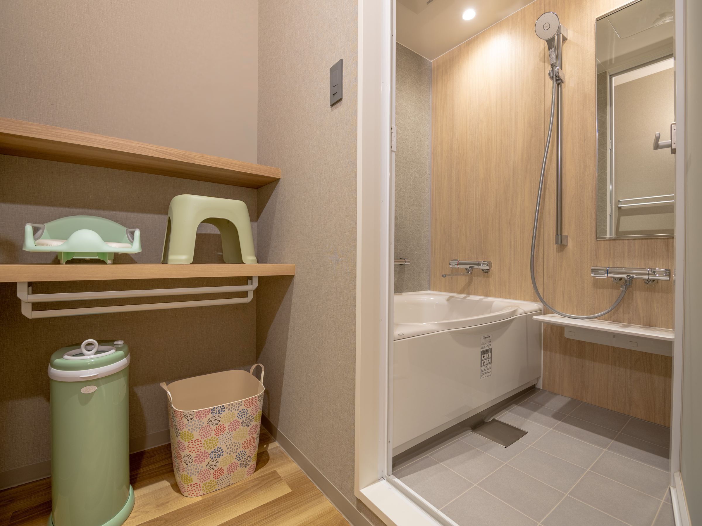 A bathroom with a shower, toilet, and sink. There are shelves with a green chair and a trash can.