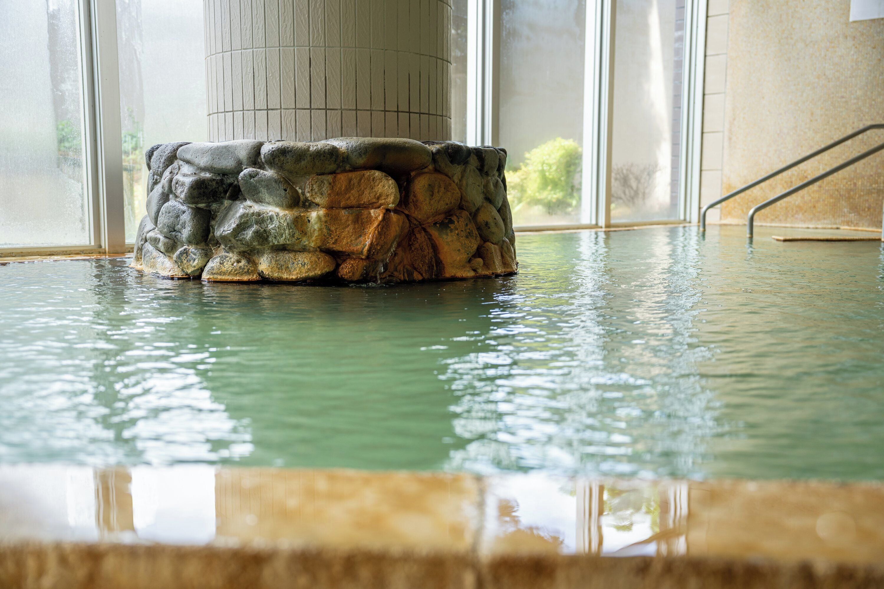 Estructura de piedra en una zona de piscina con vista a un edificio y árboles.