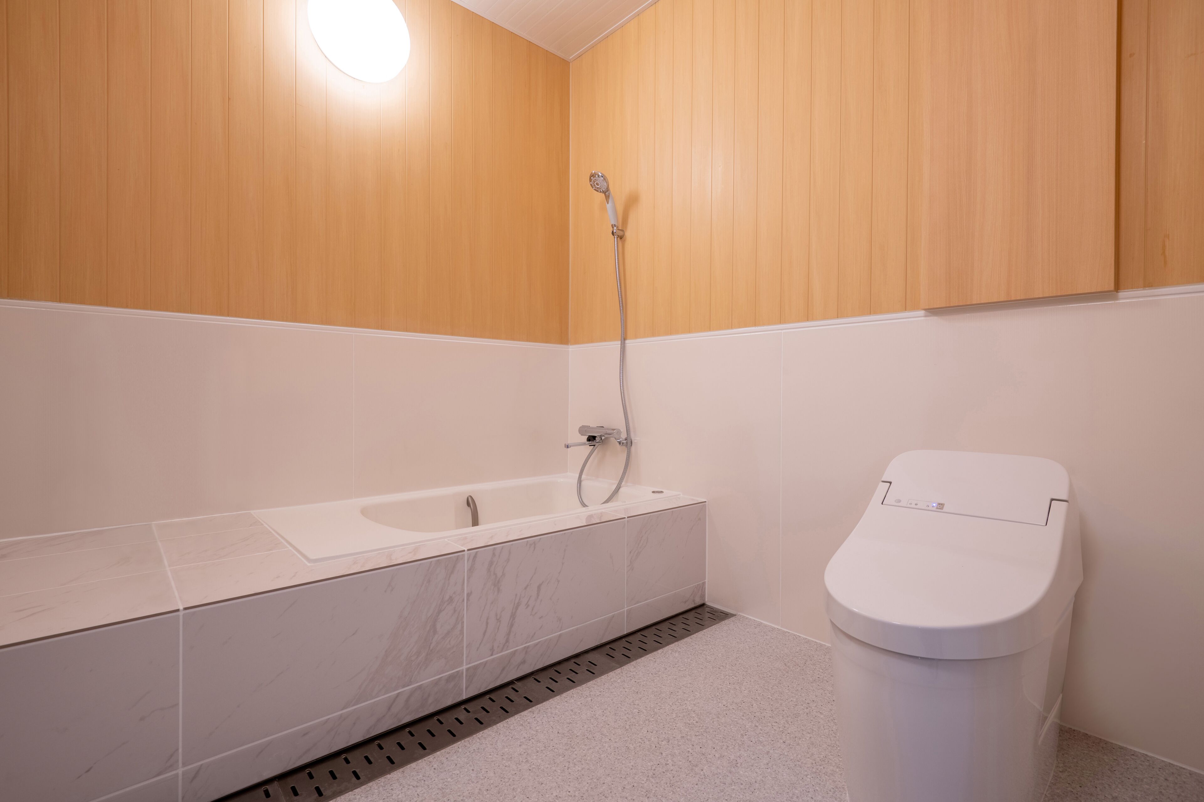 A modern bathroom with a white bathtub, a showerhead, and a toilet.