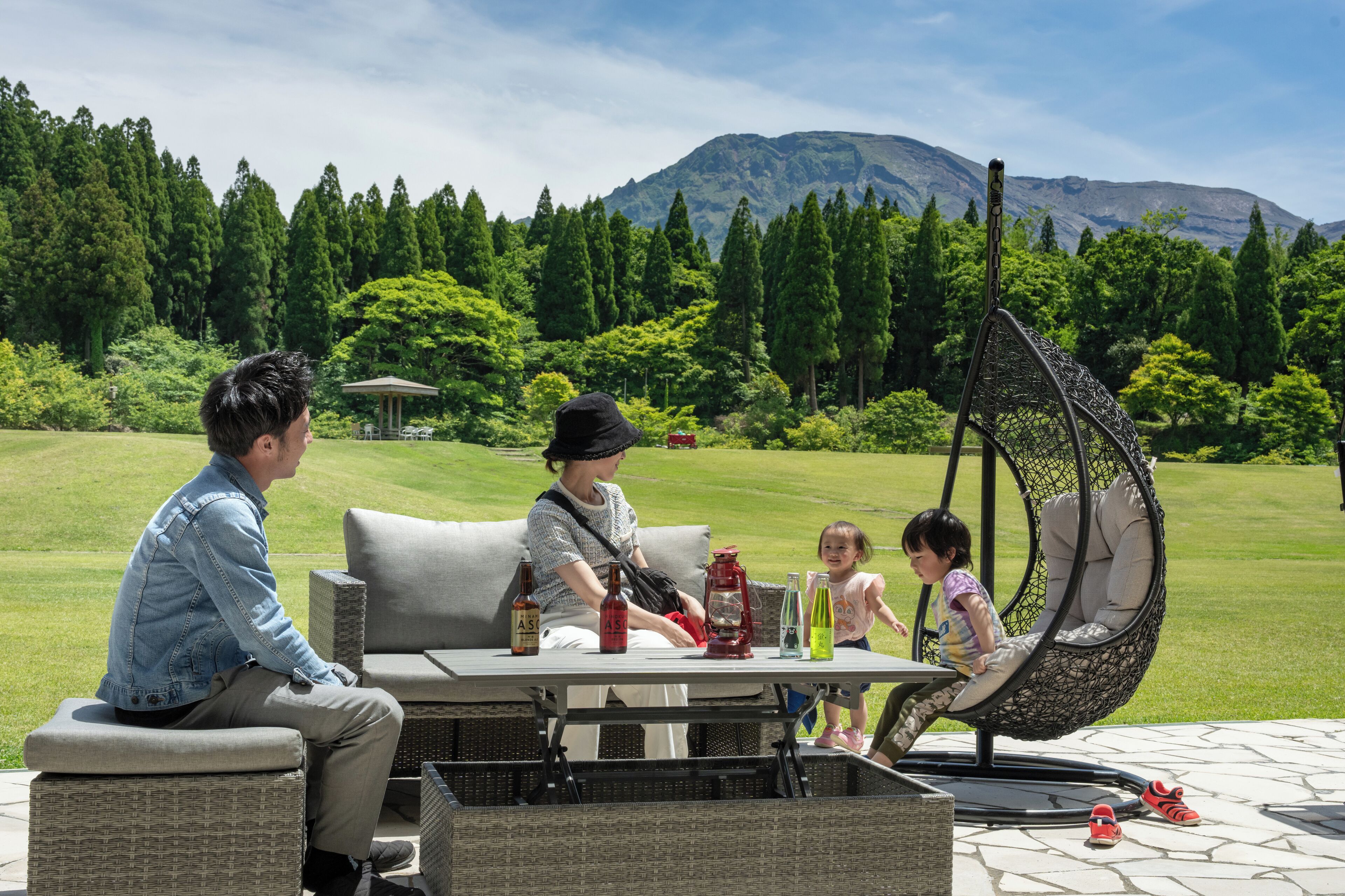 A patio with wicker furniture, a swing chair, and a table with bottles.