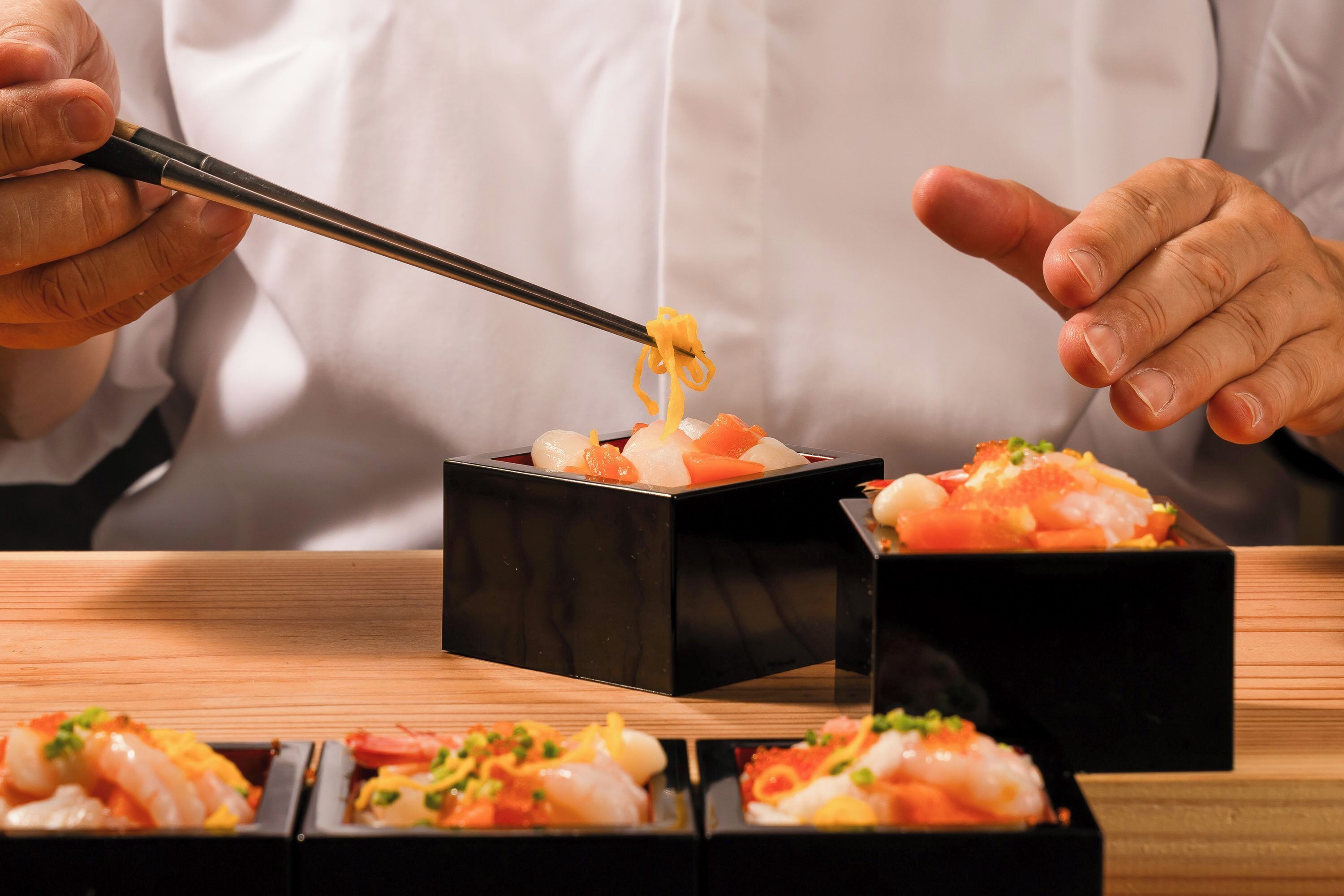 A person using chopsticks to pick up food from a black box.