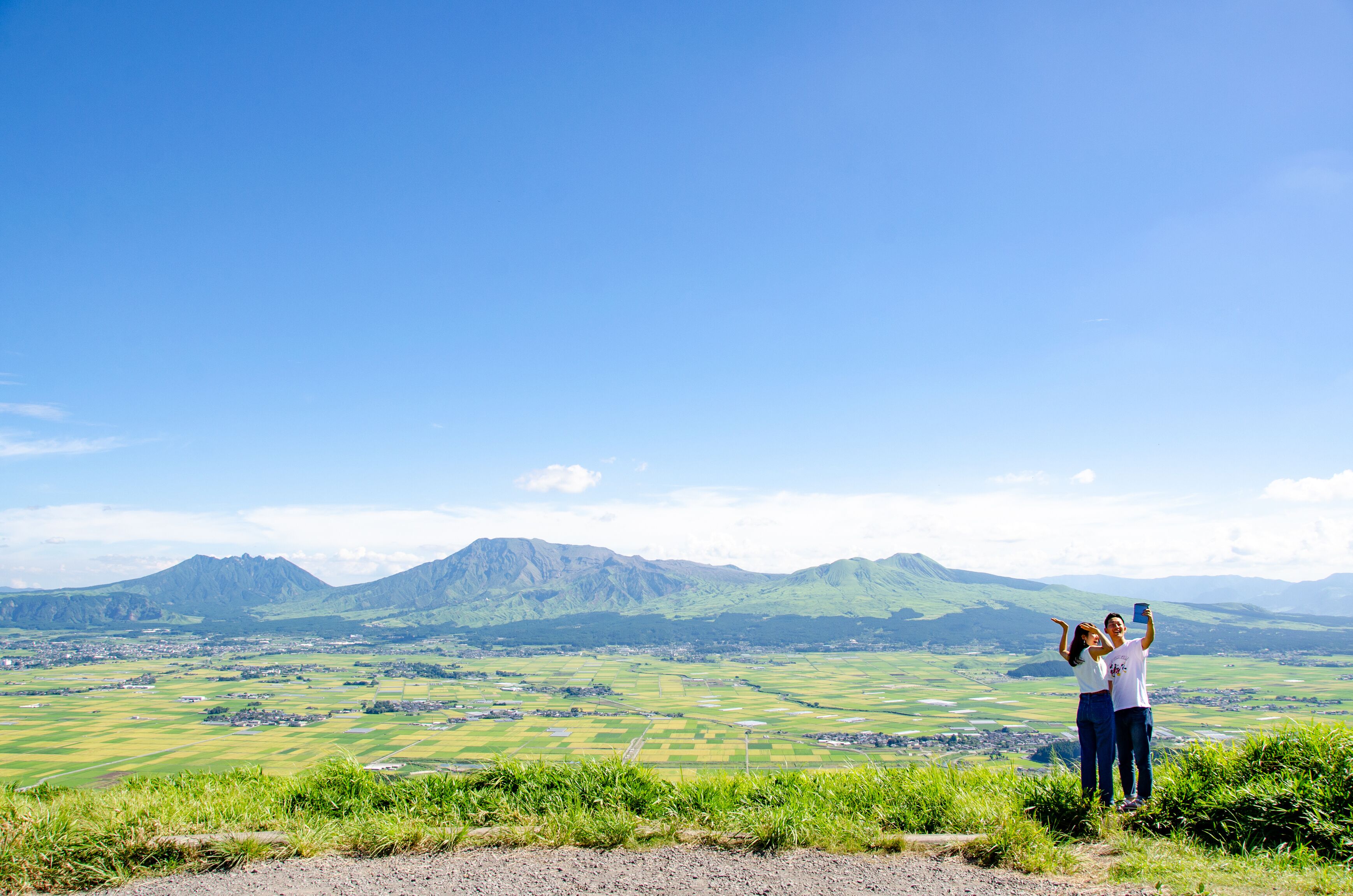 Una coppia si fa un selfie con una vista panoramica su campi verdi e montagne sullo sfondo.