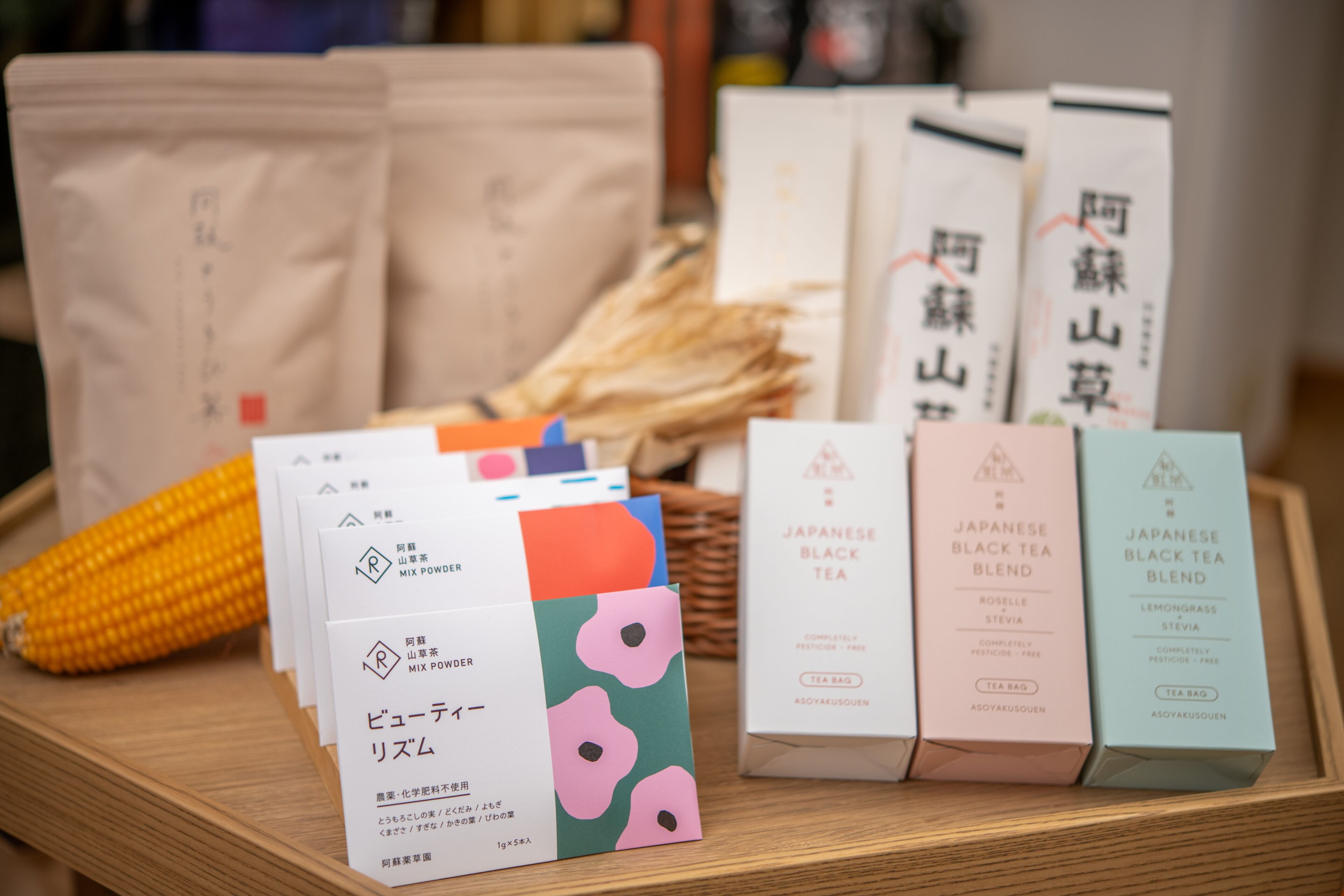 Ein Holztablett mit verschiedenen Tee-Produkten, darunter eine japanische Schwarztee-Mischung und Mix-Pulver, sowie einer Ohrkolbenmaissilage.