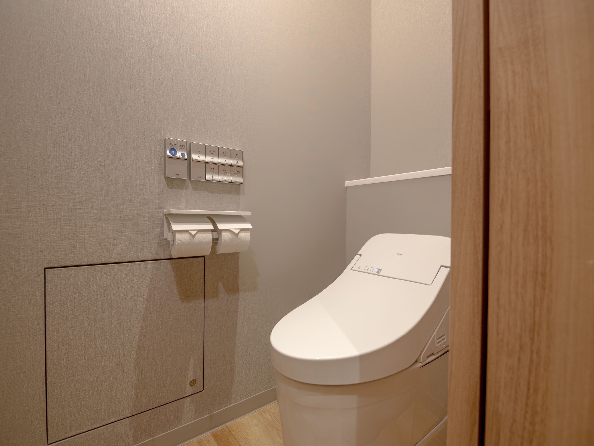 A modern bathroom with a toilet, a paper towel dispenser, and a flush button.