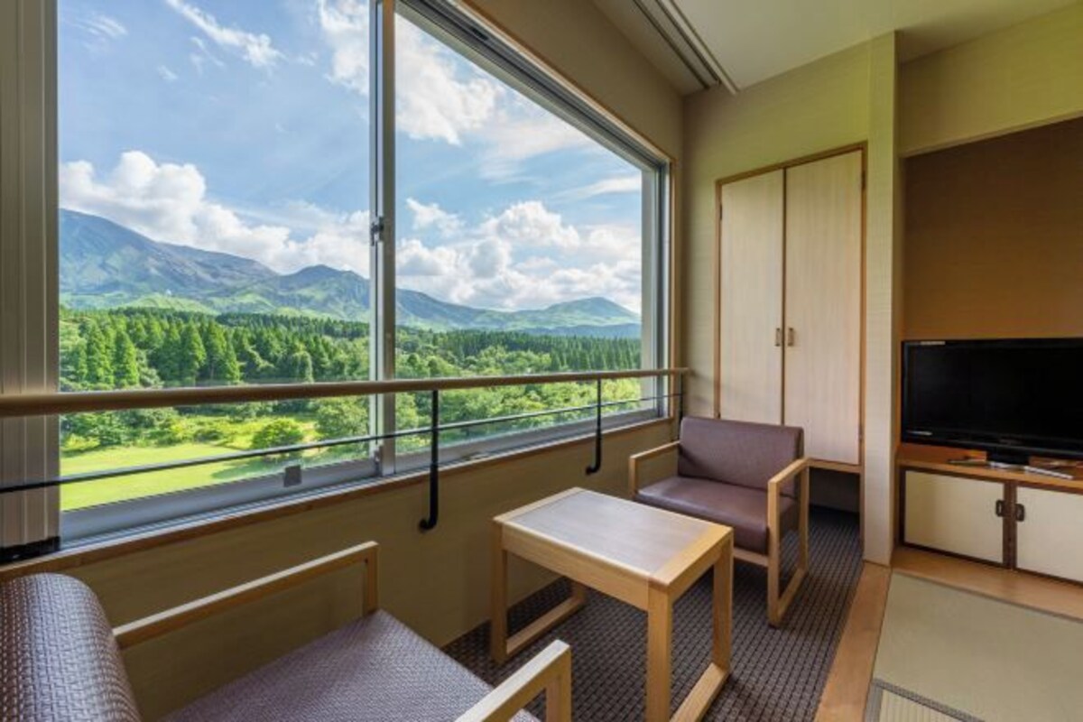 Habitación de hotel con un ventanal que ofrece vistas a la montaña, un televisor y una zona de estar con una mesa.