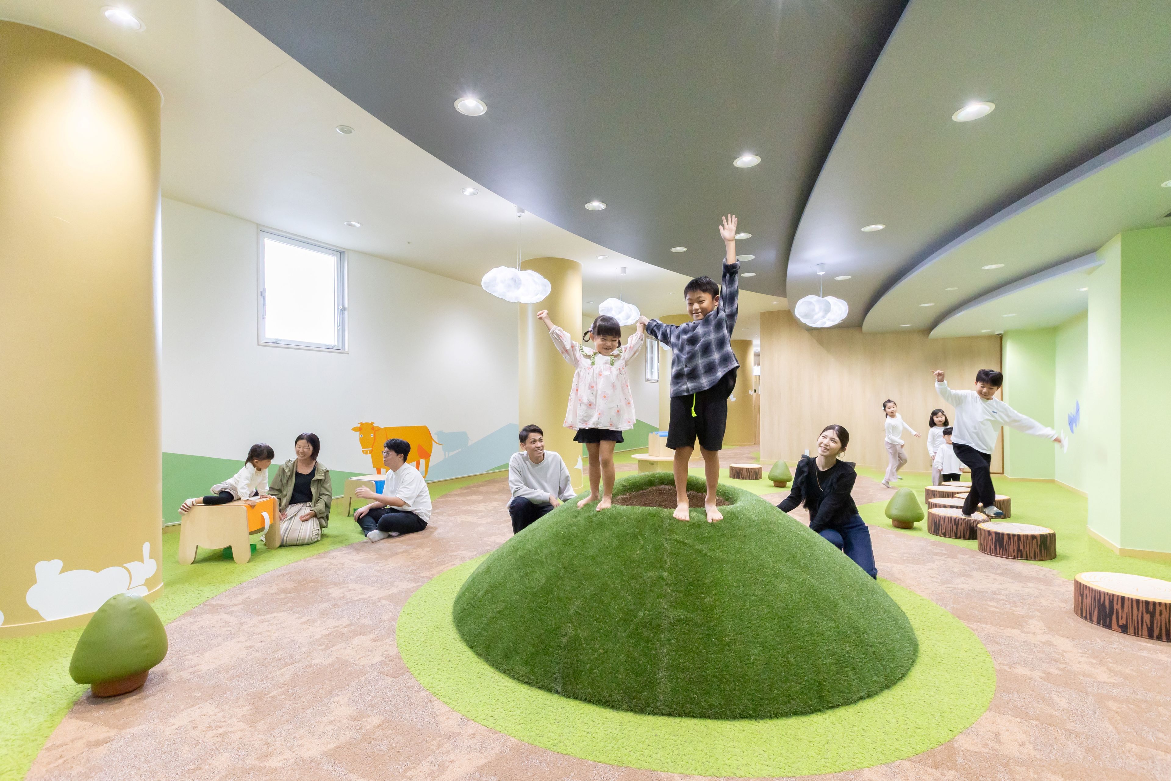 A children's play area with artificial grass, wooden play structures, and a large window.