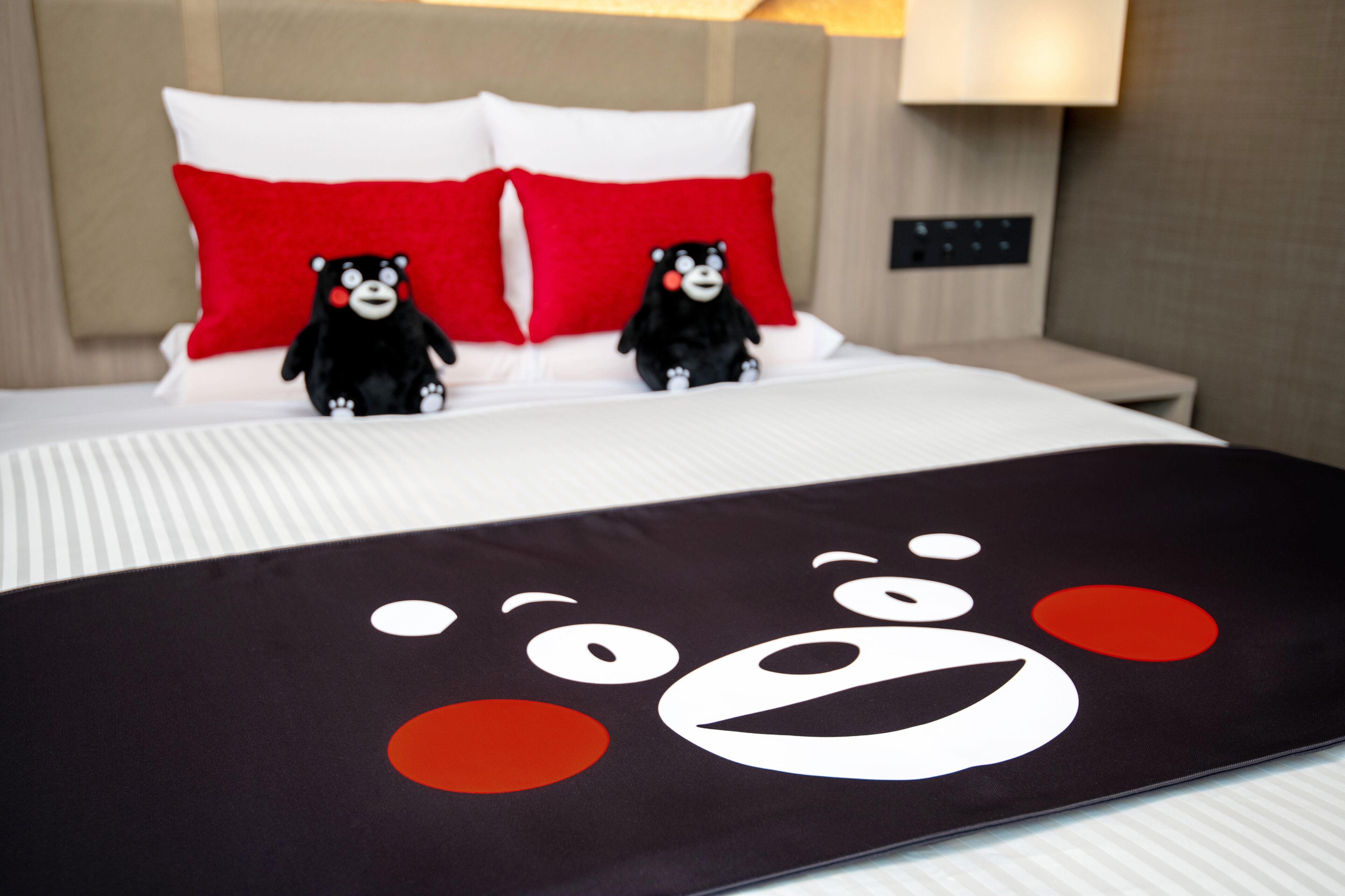 A bed with two plush toys, a pillow with a bear face, and a bedspread with a bear face design.