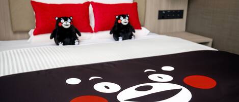 Una cama con dos peluches, un almohadón con cara de oso y una colcha con diseño de oso.
