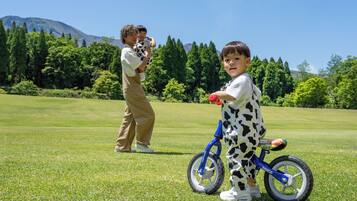 Un champ verdoyant où l’on voit un enfant sur un tricycle bleu et un adulte qui tient un enfant dans ses bras.