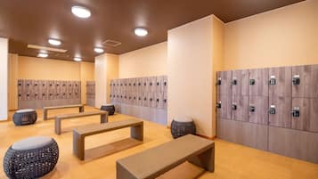 Un vestuario moderno con bancos de madera, taburetes redondos y varios casilleros.