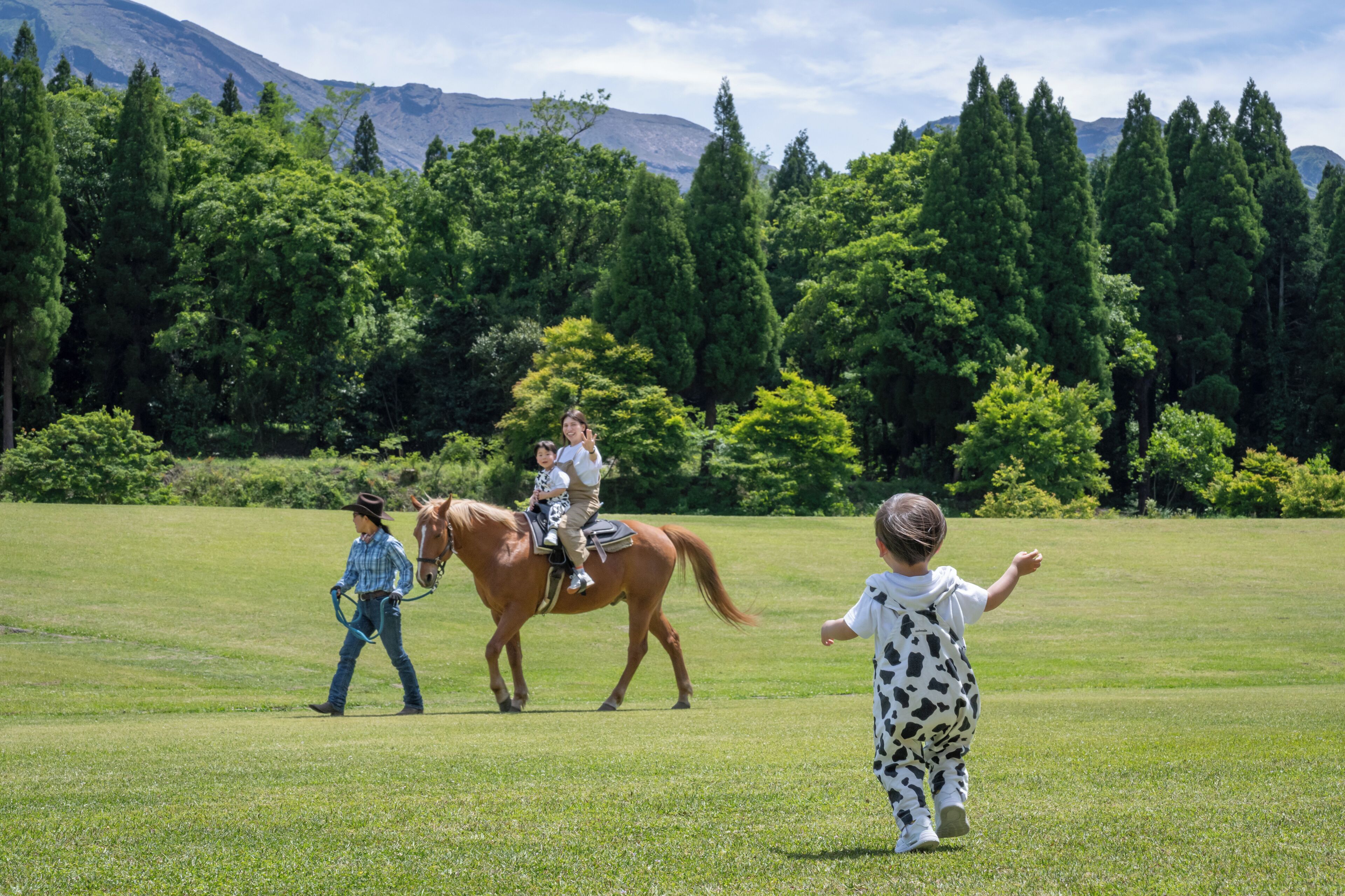 A grassy field with a horse and two people, one riding and one walking a horse.