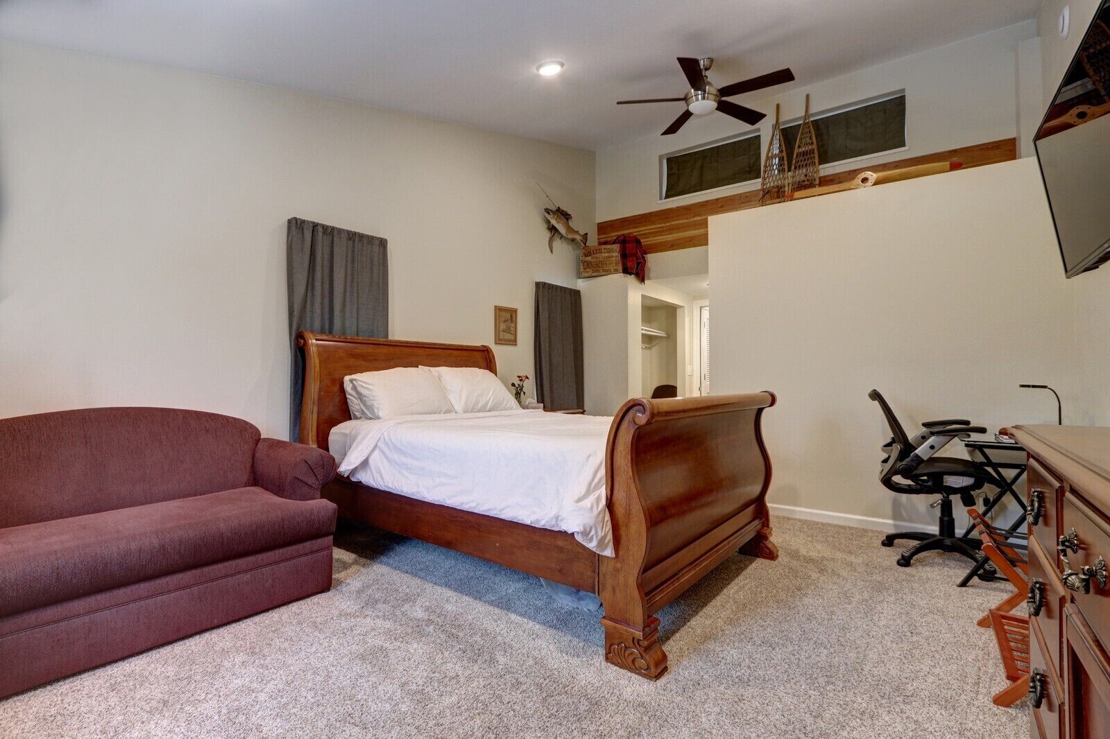 Une chambre à coucher avec un lit en bois, un fauteuil rouge, un bureau avec une chaise et un ventilateur de plafond.