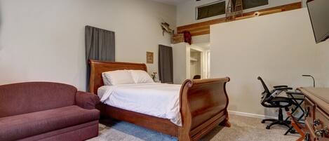 Une chambre à coucher avec un lit en bois, un fauteuil rouge, un bureau avec une chaise et un ventilateur de plafond.