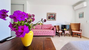 Un salon avec un canapé, des fauteuils, une table ornée d’un vase de fleurs et un tableau accroché au mur.