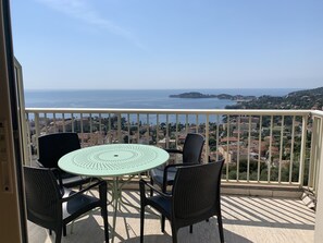 A balcony with a table and chairs, overlooking a coastal cityscape.