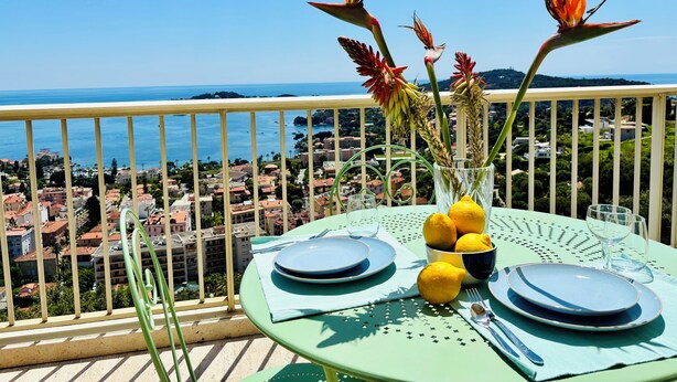 Une table dressée sur un balcon, avec vue sur la mer et la ville.