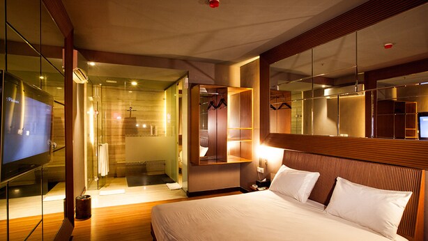 Habitación de hotel con una cama grande, vestidor, baño con ducha de vidrio y un televisor a la izquierda.