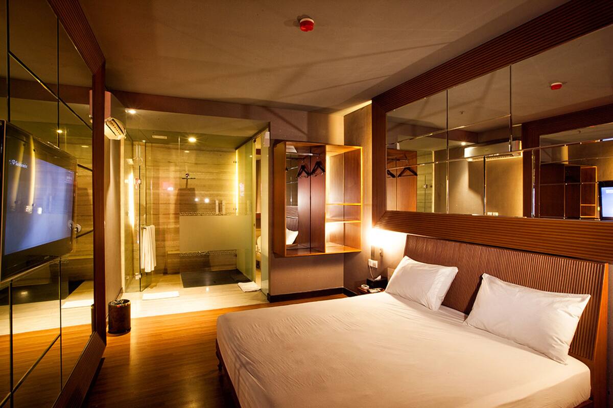 A hotel room with a large bed, a walk-in closet, a bathroom with a glass shower, and a television on the left side.