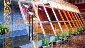 Un edificio moderno con fachada de vidrio, diseños decorativos y una serie de macetas con plantas verdes.