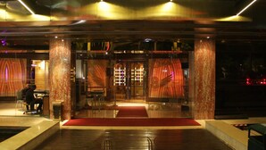 Entrada de hotel con alfombra roja, pilares grandes y puerta de vidrio con diseños decorativos.