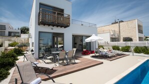 Et moderne hus med to etager, en swimmingpool, udendørs møbler og en balkon.