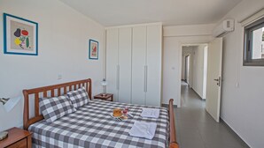 Et soveværelse med ternet sengetæppe, et natbord med lampe, et indrammet billede af grøntsager og en garderobe med skydedøre.