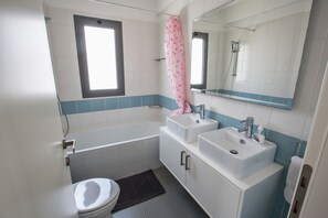 Un baño con bañera, dos lavamanos, inodoro y ventana.