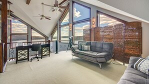 A spacious loft bedroom with large windows, a ceiling fan, a desk, and a sofa. - Luxe Group Home w/ Boat Dock in Lake of the Ozarks (Kaiser)