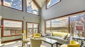 A spacious living room with large windows, a sofa, chairs, and a coffee table. - Luxe Group Home w/ Boat Dock in Lake of the Ozarks (Kaiser)