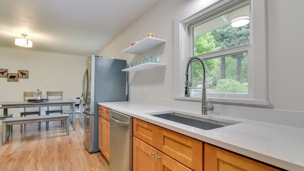 A modern kitchen with a stainless steel refrigerator, wooden cabinets, a white countertop, and a window with a view of greenery. - Downtown Home w/ Patio - Walk to Shops & Dining! (Stevenson)