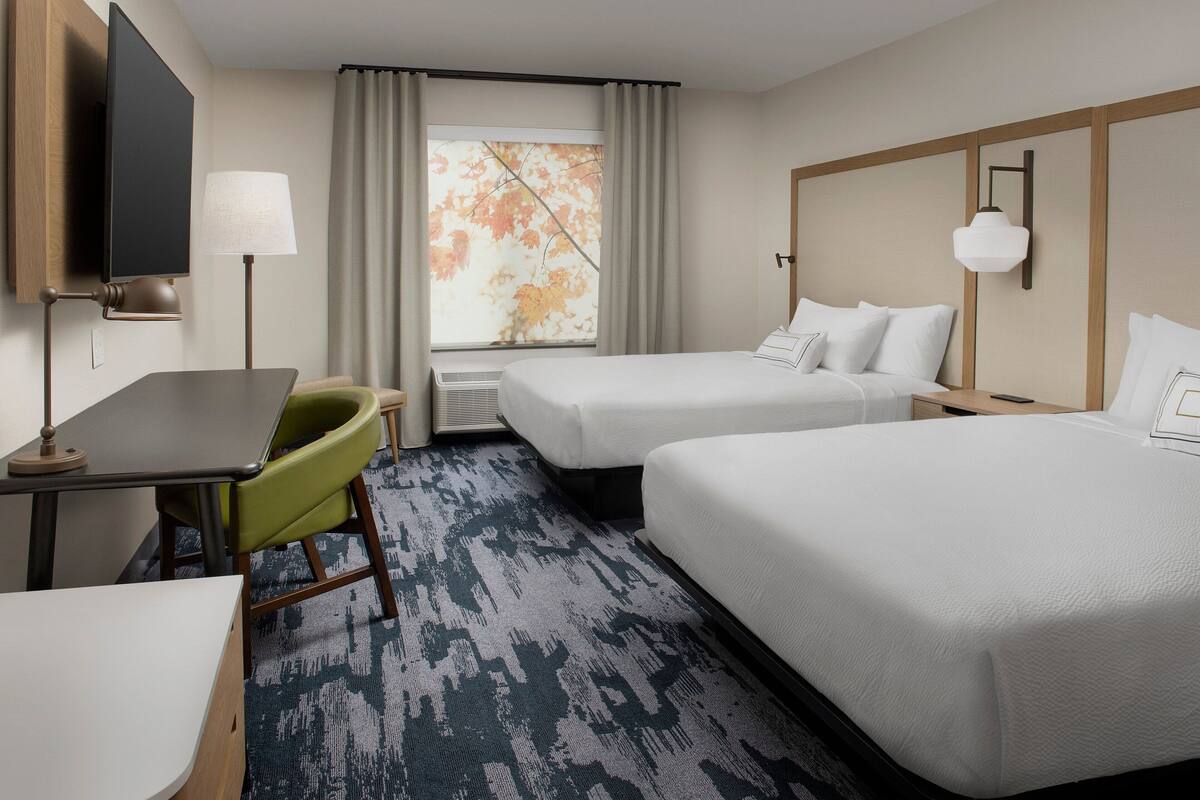 A hotel room with two beds, a desk, a chair, a TV, and a window with curtains.
