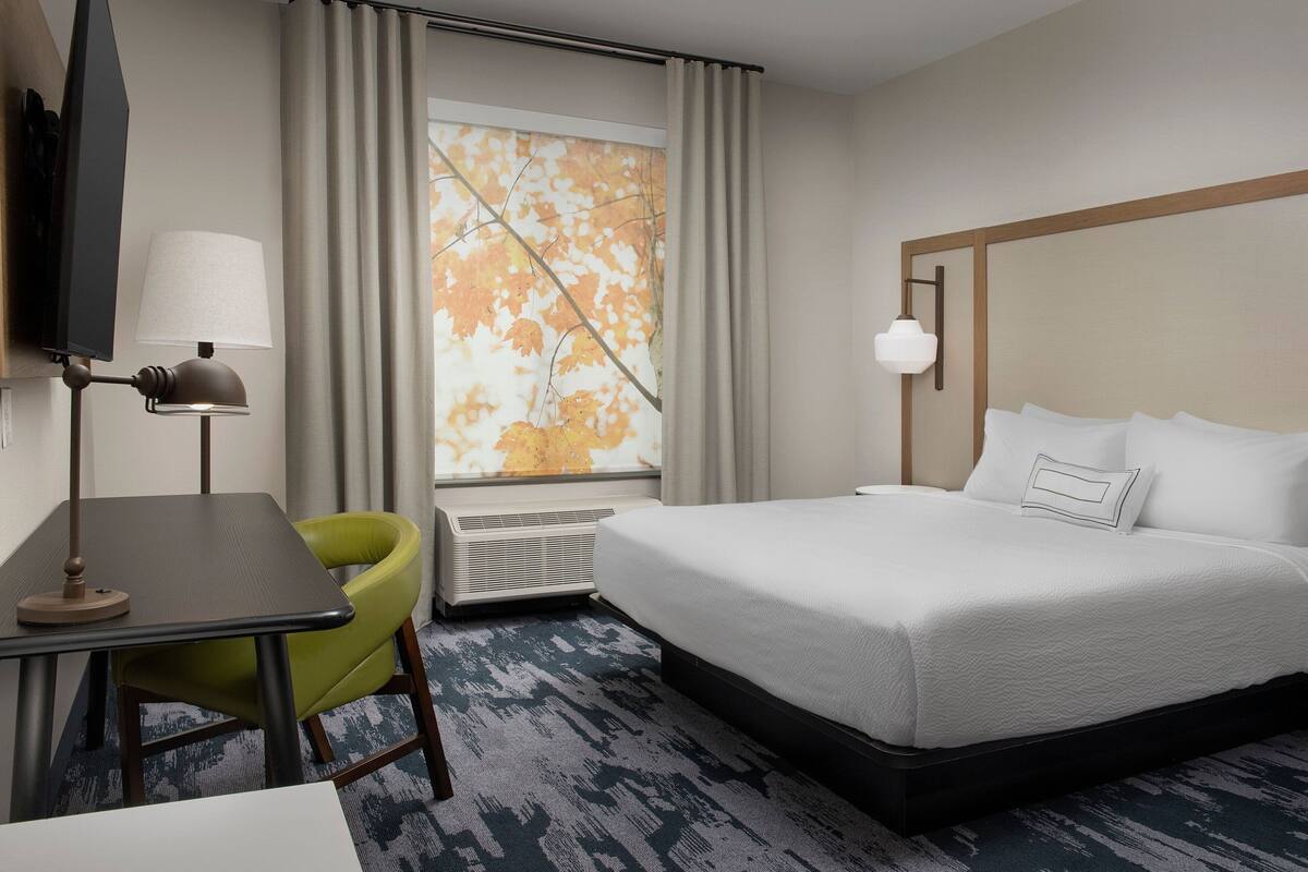 A hotel room with a bed, a desk, a chair, a TV, and a window with curtains.