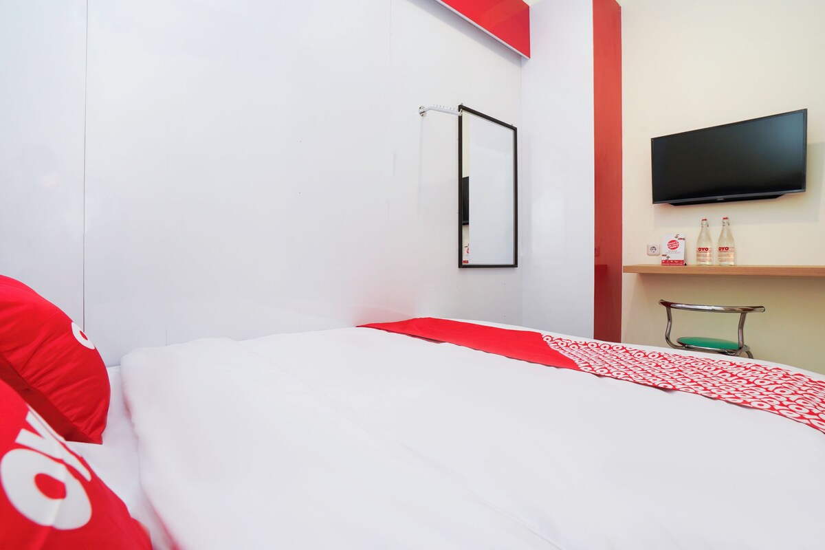 A hotel room with a bed, a TV mounted on the wall, and a small table with bottles.