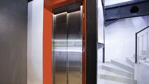 A modern elevator with metallic doors, adjacent to a staircase with glass railings. - SUPER OYO Flagship 3688 Pot Art (Surabaya)