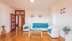 Una sala de estar con piso de madera, sofás blancos con cojines azules, una mesa de centro y un jarrón con flores.