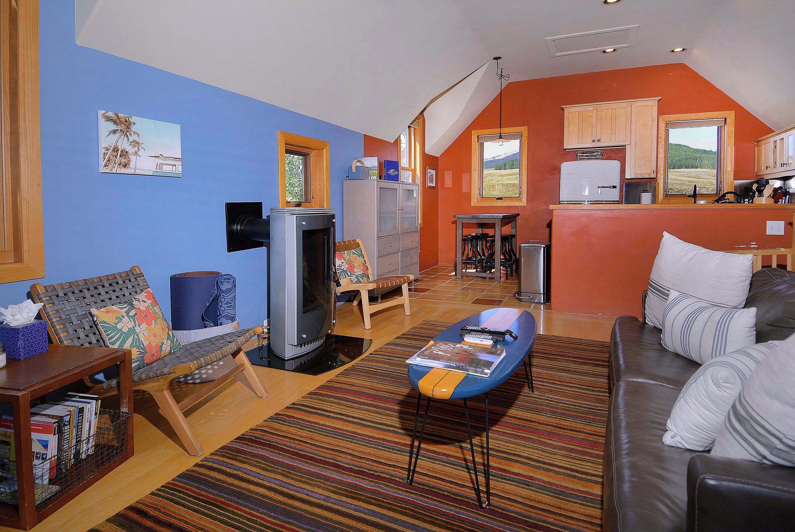 A living room with a sofa, a television, and a coffee table. There is a kitchen area with a refrigerator and a window.
