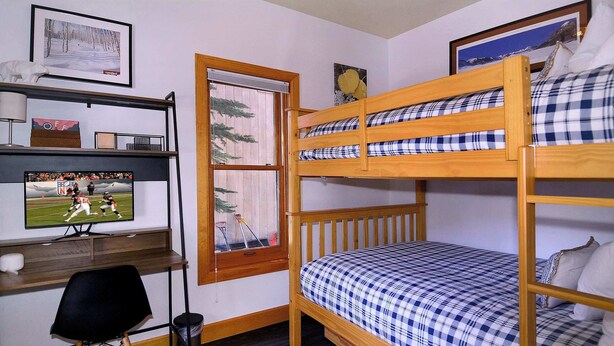 A bunk bed with a checkered bedspread, a desk with a computer monitor, and a window with a view of trees. - The Surf Shack, On shuttle route, EV charger (Crested Butte)