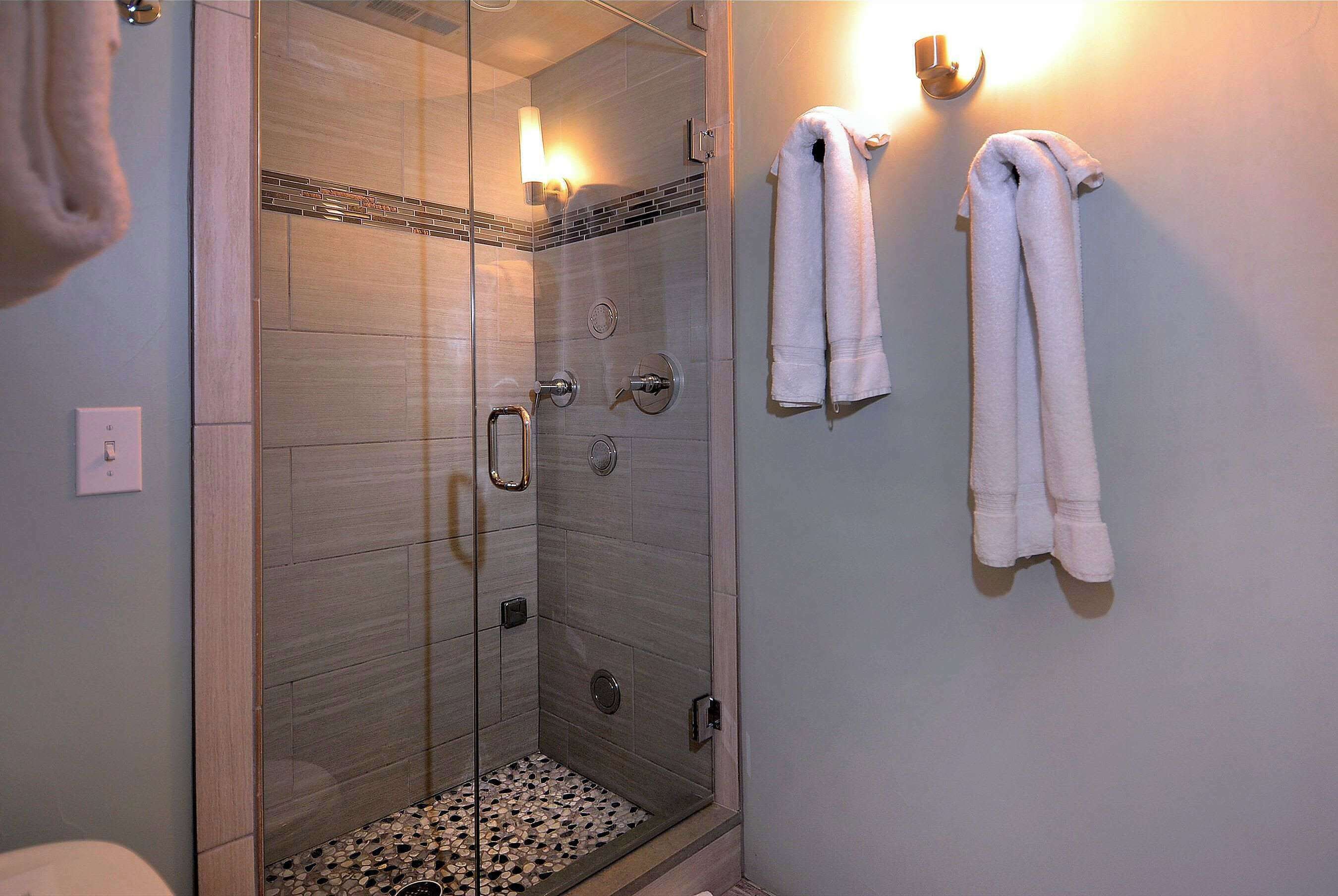 A glass-enclosed shower with a tiled floor, a towel rack with two towels, and a wall-mounted light fixture.