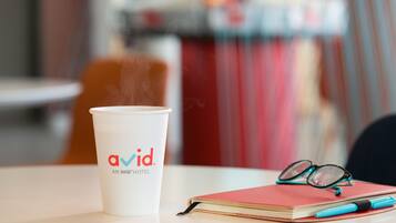 A white cup with "avid" logo, a red notebook, and a pen on a table.