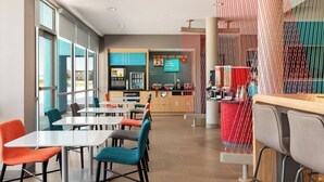 A modern restaurant with a bar area, seating with colorful chairs, and a view through large windows. - avid hotel Sioux City - Downtown by IHG (Sioux City)