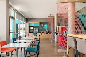 A modern restaurant with a bar area, seating with colorful chairs, and a view through large windows. - avid hotel Sioux City - Downtown by IHG (Sioux City)