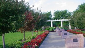 A pathway lined with stone markers and a pergola structure amidst a garden with various plants and trees.