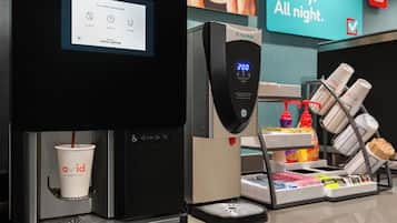 Máquina de café a servir café numa chávena, um mostrador digital e uma área de café com diversos artigos.
