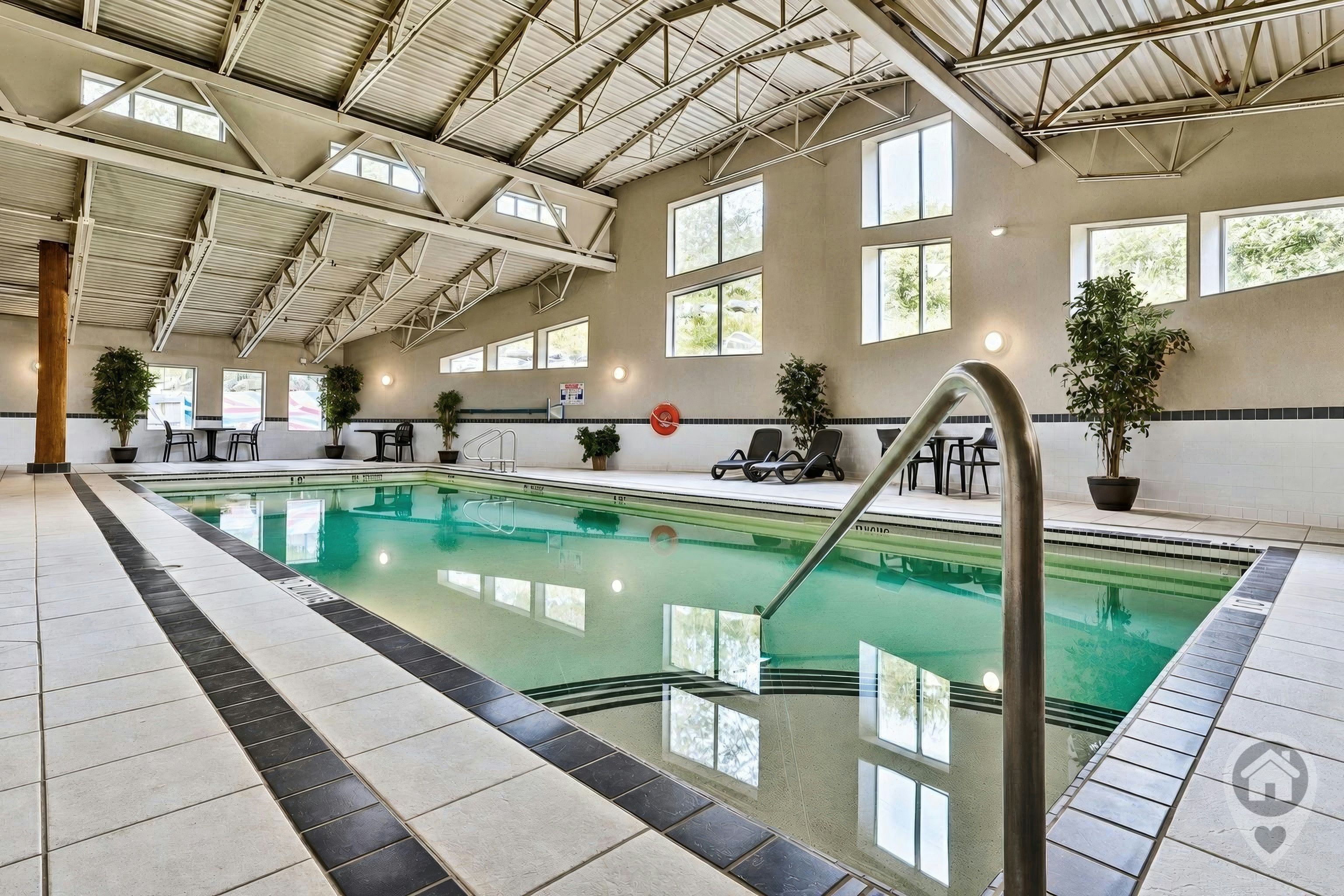 Une piscine intérieure à l’eau claire, entourée d’un sol carrelé et agrémentée de plantes en pot.