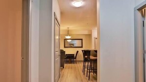 Un corridoio stretto con pavimento in legno che conduce a una sala da pranzo con tavolo e sedie.